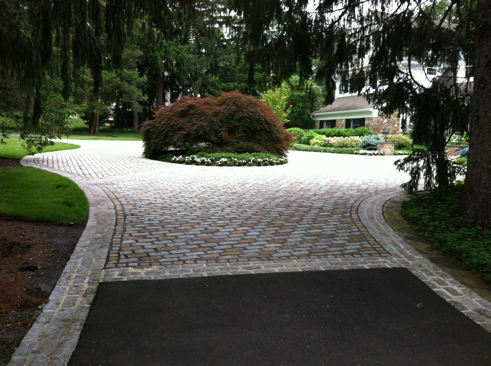 Cobblestone apron meeting an asphalt drive with a weeping-maple island and hemlock frame