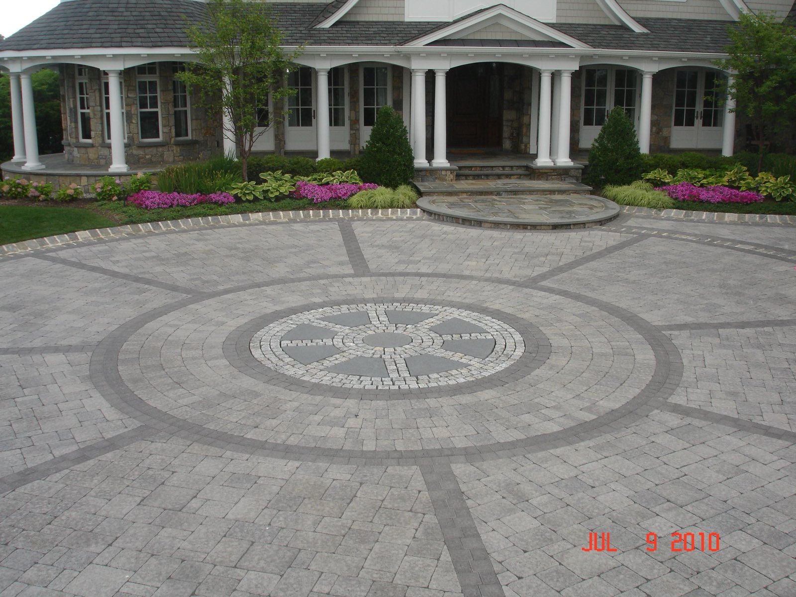 Ground-level circular paver motor-court with a compass medallion and a columned stone porch