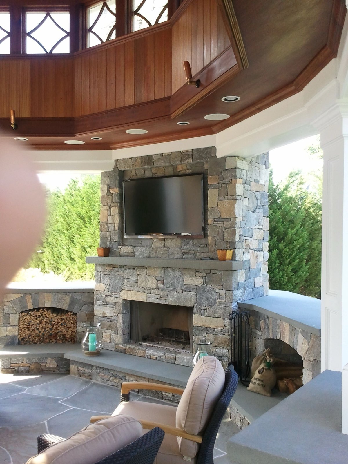 Covered outdoor living room with a full stone fireplace and coffered wood ceiling